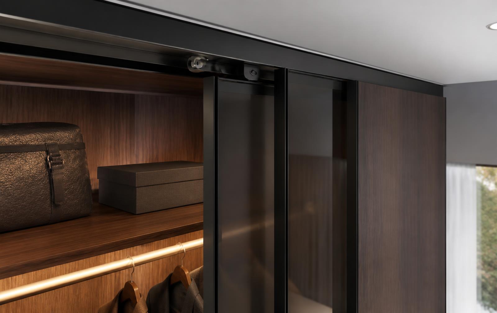 Top-hung sliding wardrobe system with matte black anodised aluminium track, smoked glass and walnut door panels in a luxury bedroom